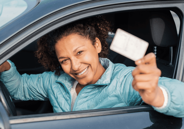 Woman smiling in a car holding a drivers license out of the window